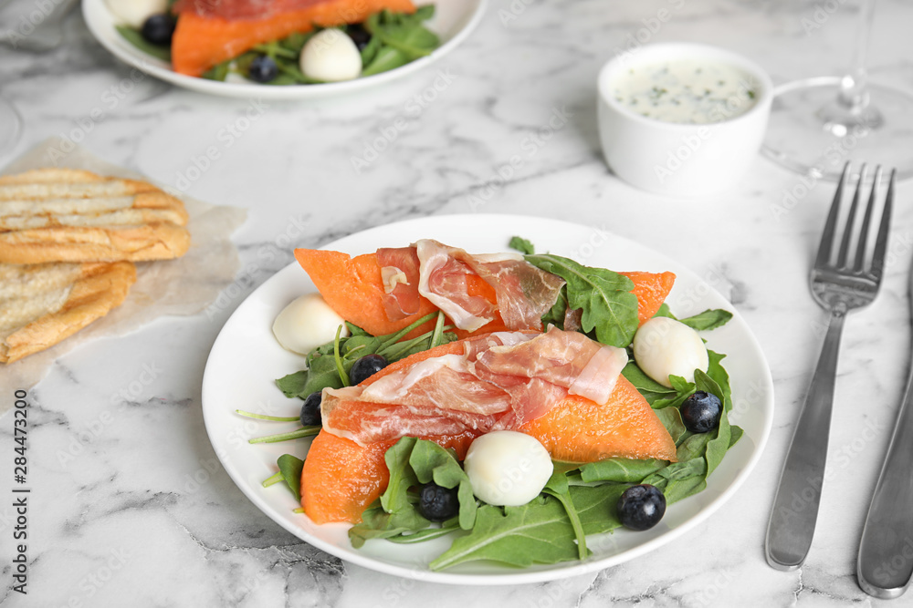 Fresh melon with prosciutto, mozzarella and arugula on marble table Fresh melon with prosciutto, mozzarella and arugula on marble table