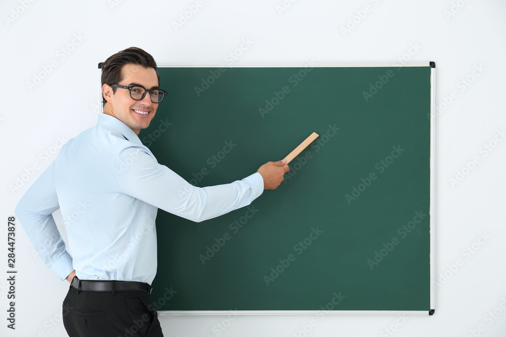 Young teacher with ruler near blank chalkboard in classroom. Space for text Young teacher with ruler near blank chalkboard in classroom. Space for text