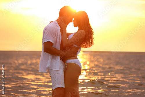 Happy young couple spending time together on sea beach at sunset