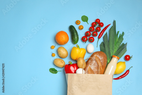 Shopping paper bag with different groceries on light blue background, flat lay. Space for text photo