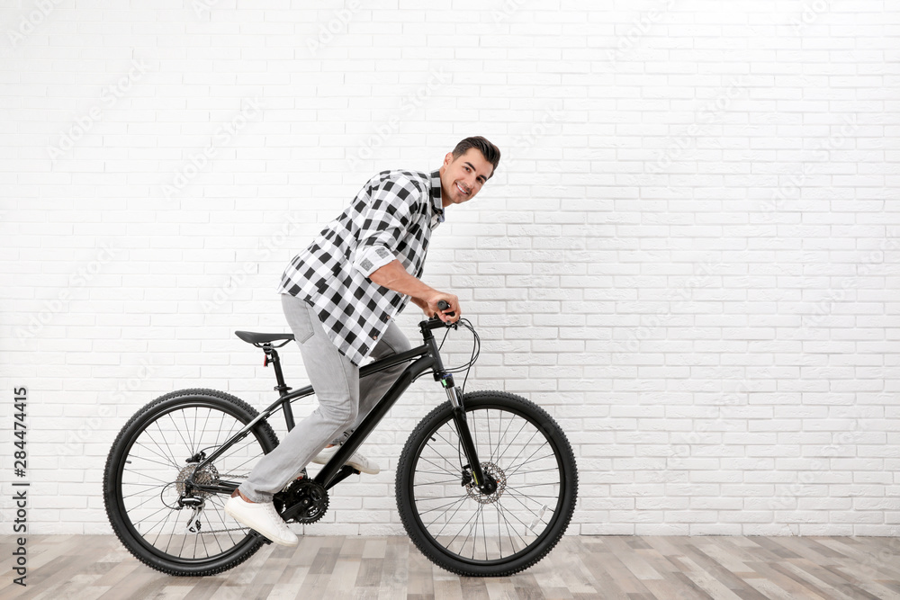 Handsome young man with modern bicycle near white brick wall indoors Handsome young man with modern bicycle near white brick wall indoors