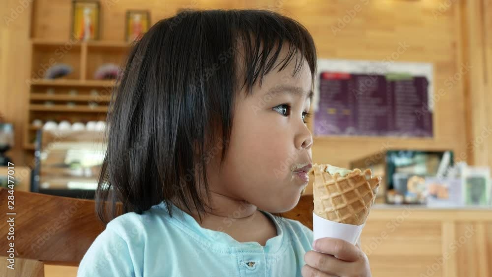 Portrait of Asian little child girl eating ice cream in cone deliciously in cafe. Portrait of Asian little child girl eating ice cream in cone deliciously in cafe.