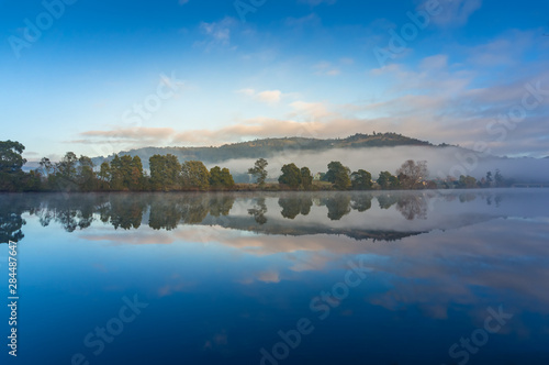 Tranquil sunrise landscape with perfect reflection of sky and trees in lake