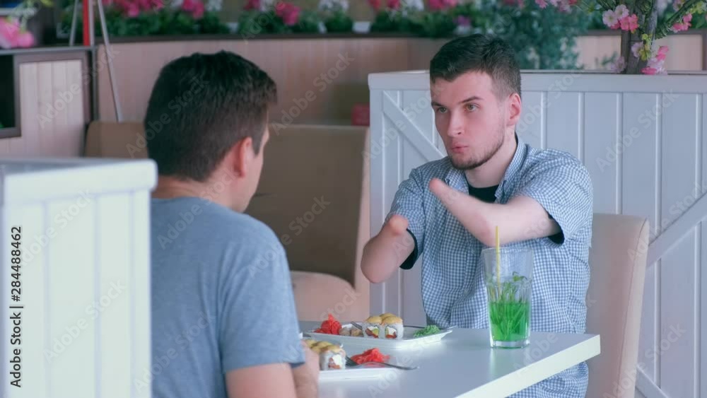 Problem of adaptation to usual life guy without wrists. Disabled man with two amputated stump hands meets friend and talks having lunch in cafe. Friend support communication. Person with disabilities. Problem of adaptation to usual life guy without wrists. Disabled man with two amputated stump hands meets friend and talks having lunch in cafe. Friend support communication. Person with disabilities.