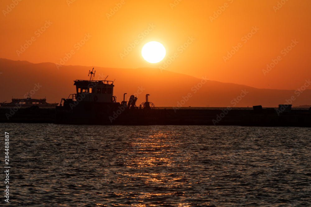 Amazing sunset in the mountains around Izmir. Taken at the waterfront in Konak district with the silhouette of a boat and the ocean.