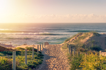 Fototapete Abstieg zum Strand Strandeingang mit Wellen bei Sonnenaufgang  © Olga K
