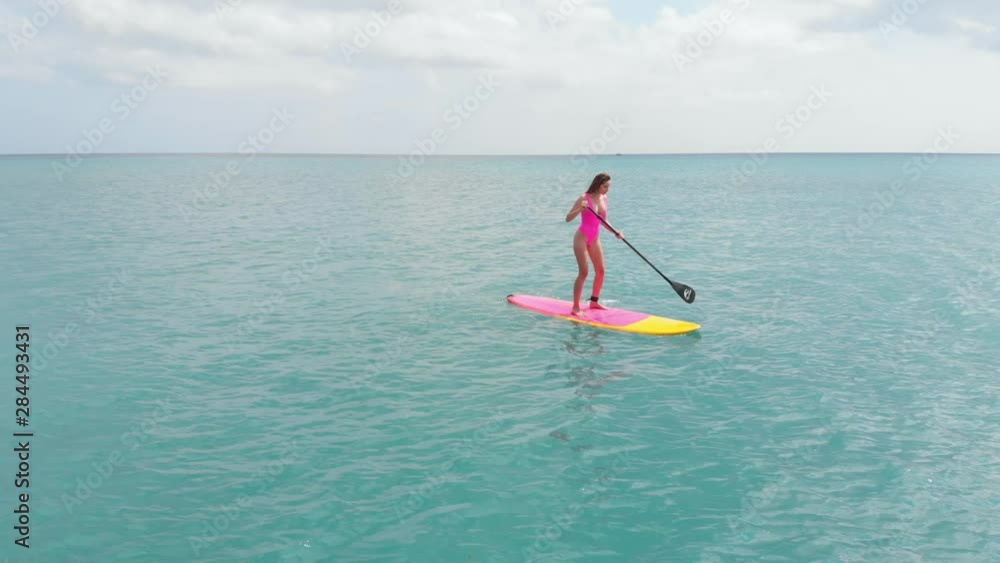 Aerial view of woman on stand up paddle board in blue ocean. Aerial view of woman on stand up paddle board in blue ocean.