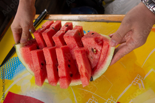Sliced water melon served desert. Close up of cut watermelon holding by chef cook hands. Healthy food dessert at picnic party outdoors. Fresh fruit serving on rind as dish