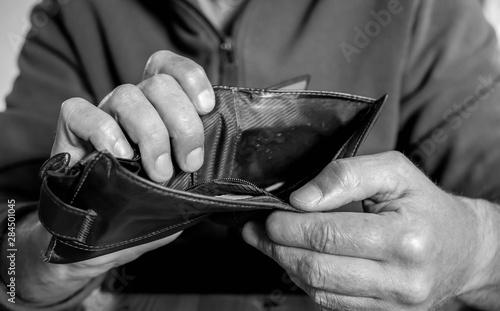 Caucasian worker  with a missing finger showing hes empty wallet, conceptual image of underpaid labour in black and white. photo