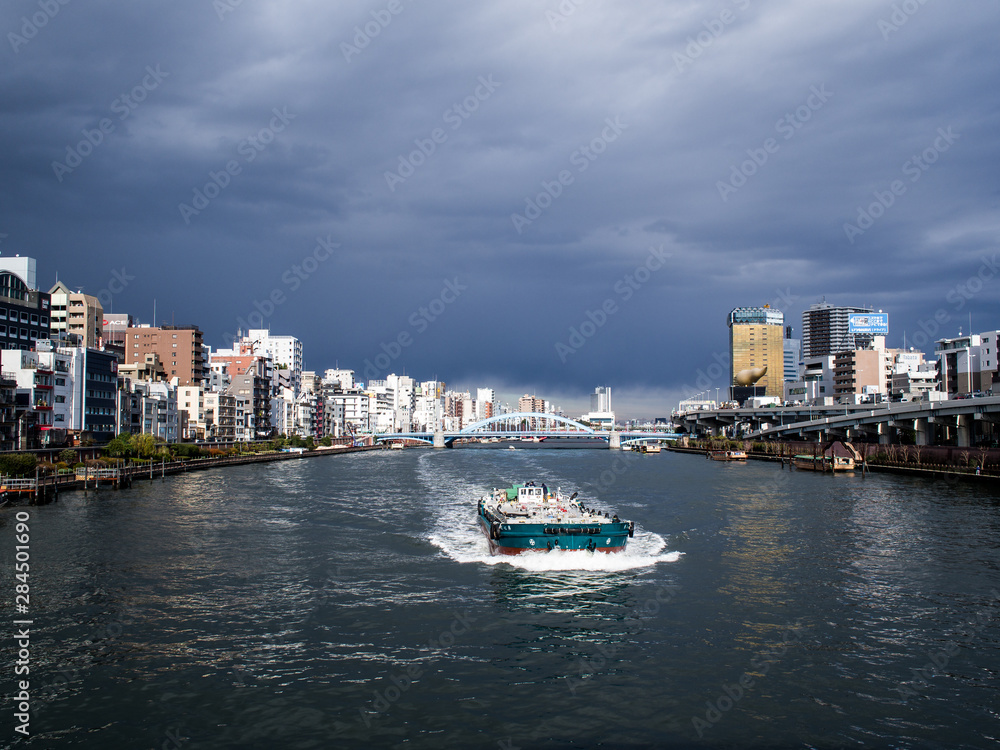 夏の曇り空の東京隅田川を行く船と川沿いの町の風景　8月