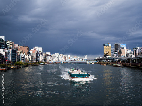 夏の曇り空の東京隅田川を行く船と川沿いの町の風景 8月