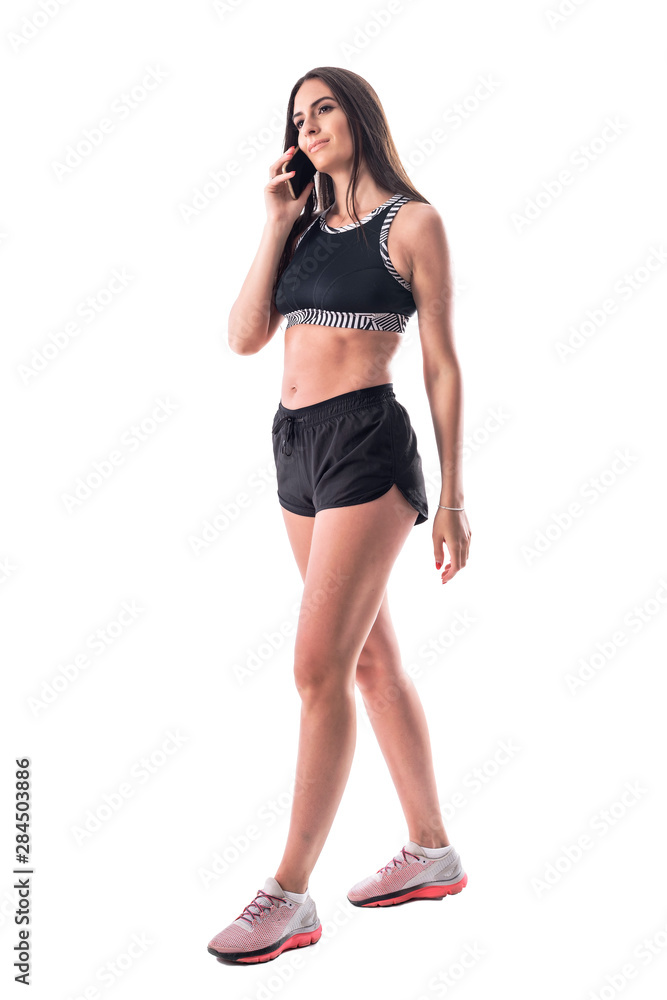 Happy young fitness athletic woman with sexy legs walking and talking on the cellphone. Full body isolated on white background. Happy young fitness athletic woman with sexy legs walking and talking on the cellphone. Full body isolated on white background.