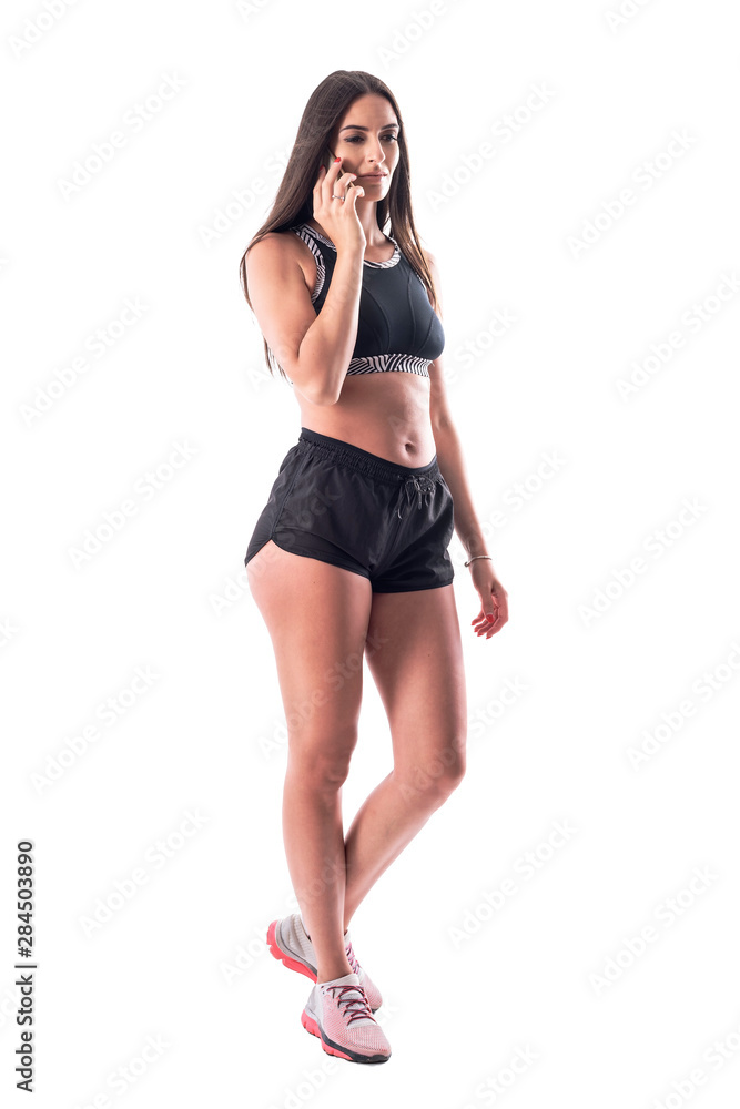 Serious athletic young sporty woman in shorts and top walking and talking on the phone. Full body isolated on white background. Serious athletic young sporty woman in shorts and top walking and talking on the phone. Full body isolated on white background.