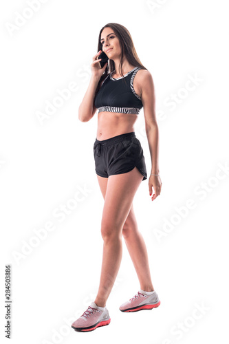 Happy young fitness athletic woman with sexy legs walking and talking on the cellphone. Full body isolated on white background. 