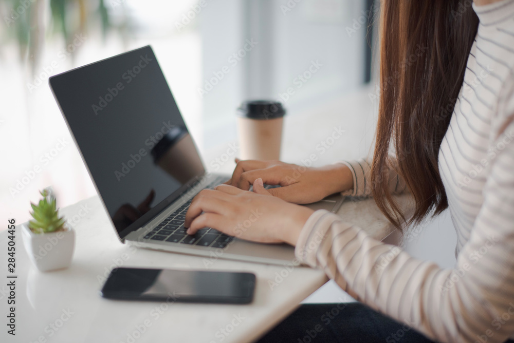 Closed up and focus on hand of young woman using a notebook laptop which put on white table and have smartphone and cup of coffee in near at cafe coffee shop. co working space concept. Closed up and focus on hand of young woman using a notebook laptop which put on white table and have smartphone and cup of coffee in near at cafe coffee shop. co working space concept.