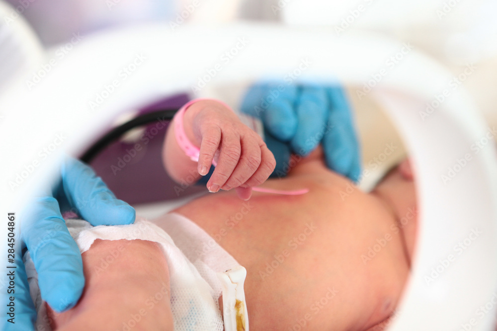 Naklejka premium Handle of a newborn baby in intensive care unit in a medical incubator. Macro photo of the hands of a doctor and the handles of a child. Newborn rescue concept. The work of resuscitation doctors.