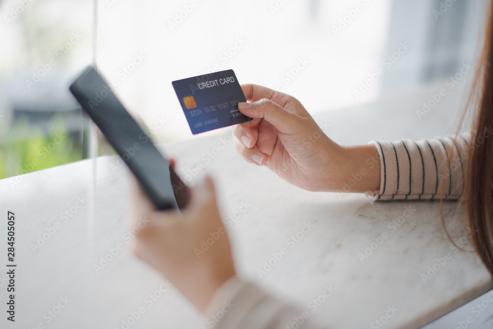 Closed up and focus on hand of young woman hold a credit card and other hand using a smart phone which is shopping online and sitting on table near big mirror at cafe. online payment concept. Closed up and focus on hand of young woman hold a credit card and other hand using a smart phone which is shopping online and sitting on table near big mirror at cafe. online payment concept.