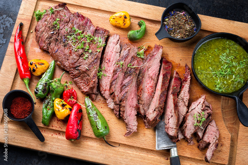 Modern design barbecue dry aged wagyu bavette de flanchet steak with chili and chimichurri sauce as top view on a wooden cutting board photo