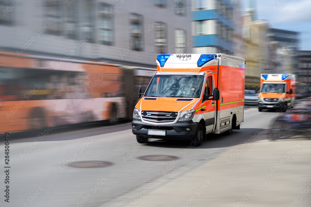 two emergency ambulances are driving fast with blue flashing light through the city, panned shot with motion blur two emergency ambulances are driving fast with blue flashing light through the city, panned shot with motion blur