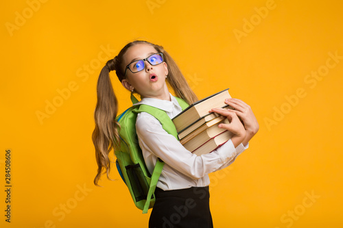 Shocked Nerdy Schoolgirl Carrying Heavy Books On Yellow Background photo
