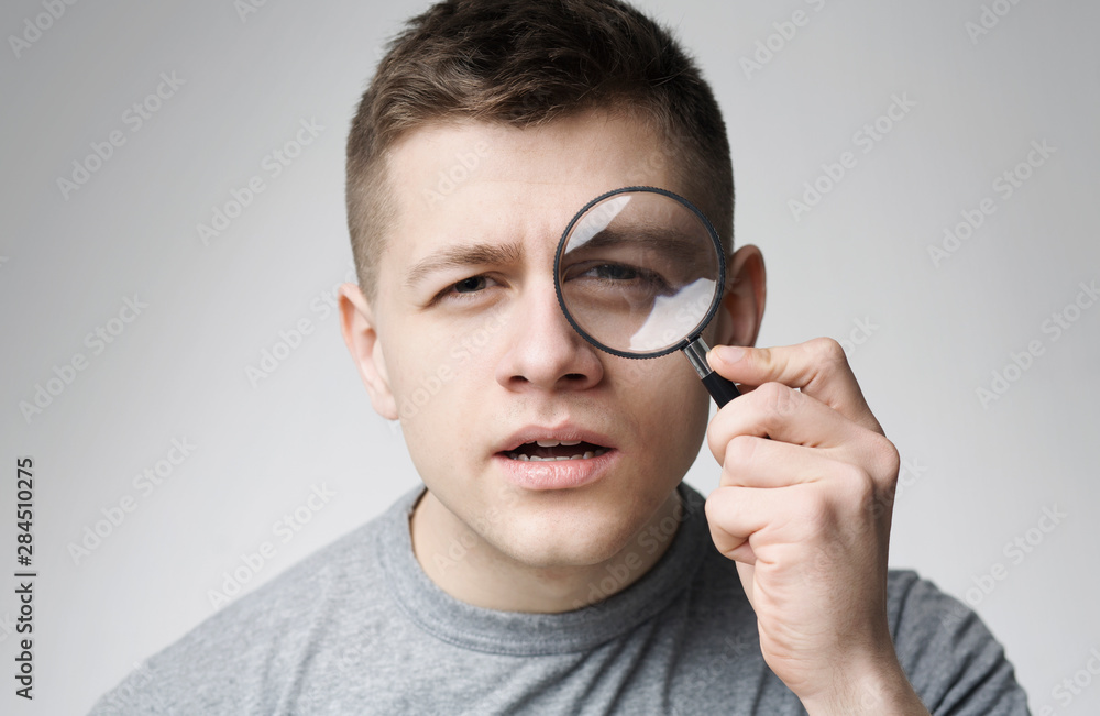 Curious young man looking through magnifying glass Curious young man looking through magnifying glass