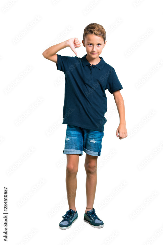 Full body of Little boy showing thumb down sign with negative expression on white background Full body of Little boy showing thumb down sign with negative expression on white background