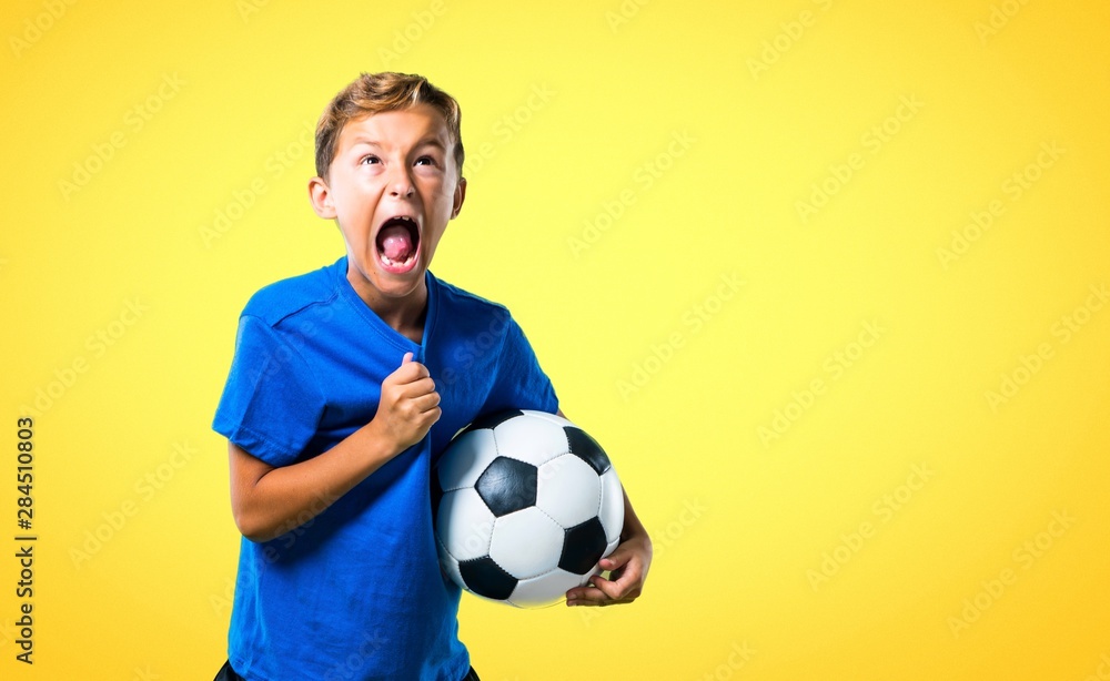 Lucky boy playing soccer on yellow background Lucky boy playing soccer on yellow background
