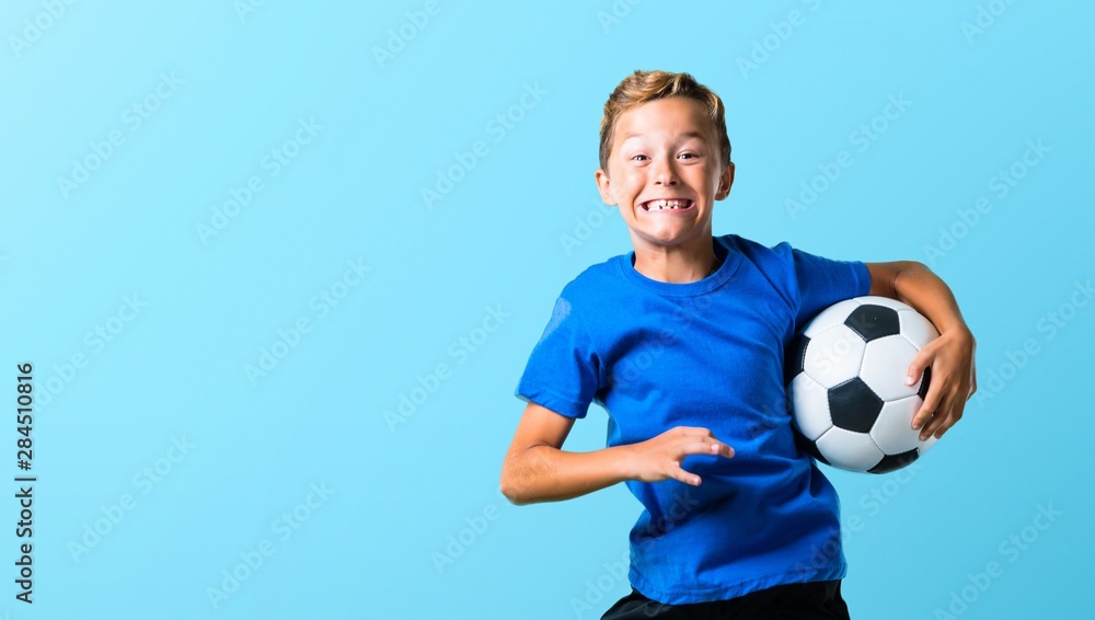 Boy playing soccer and jumping on blue background