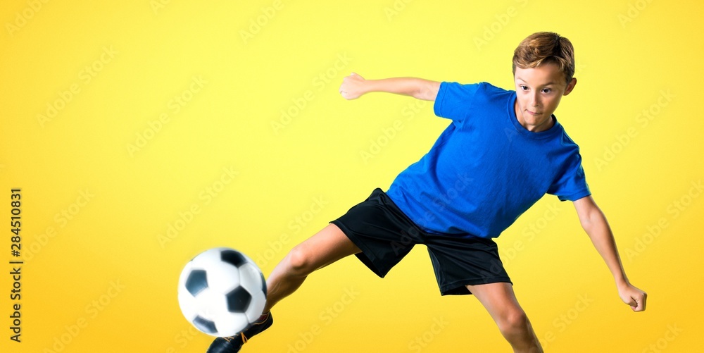 Boy playing soccer kicking the ball on yellow background