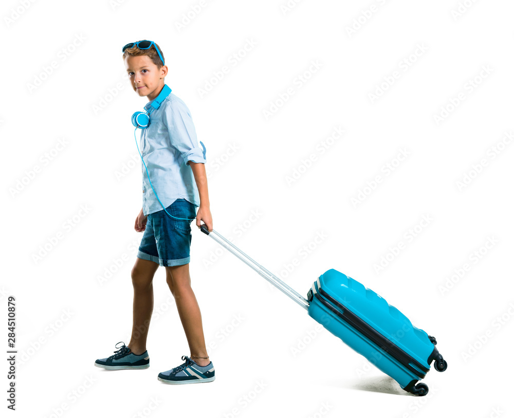 Full body of Boy with sunglasses and headphones traveling with his suitcase on isolated white background Full body of Boy with sunglasses and headphones traveling with his suitcase on isolated white background