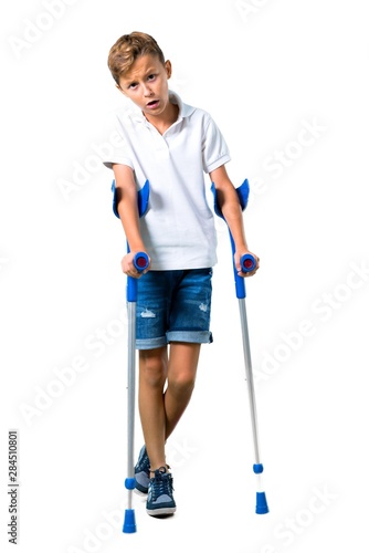 Foto Little kid with crutches on isolated white background