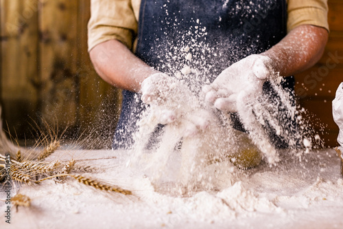 Women's hands, flour and dough.Levitation in a frame of dough and flour.A woman in an apron is preparing dough for home baking. Rustic style photo. Wooden table, wheat ears and flour. Emotional photo.
