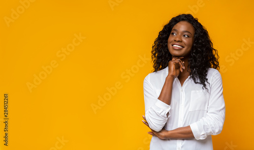 Young afro girl dreaming on yellow background