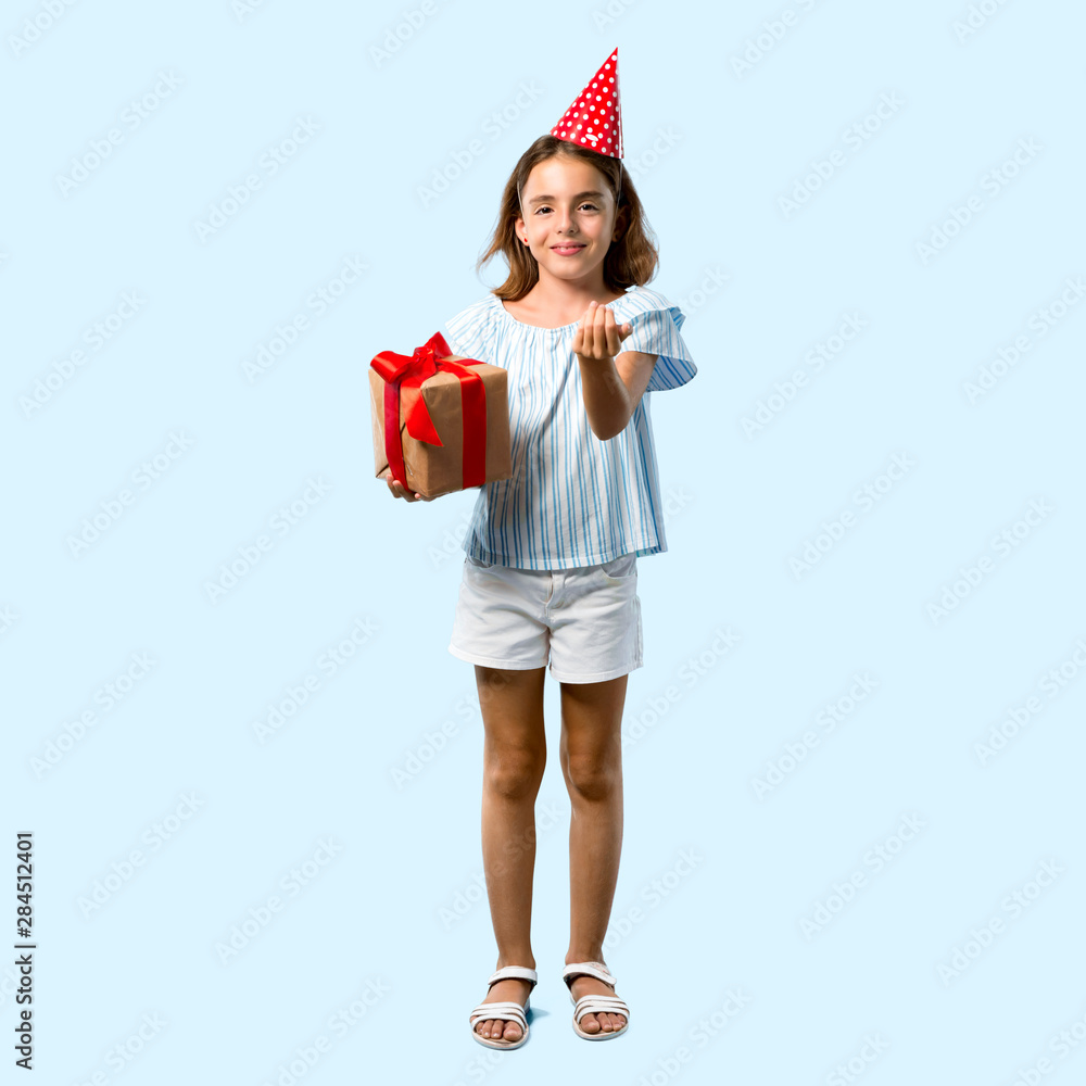 Full body of Little girl at a birthday party holding a gift presenting and inviting to come on blue background Full body of Little girl at a birthday party holding a gift presenting and inviting to come on blue background
