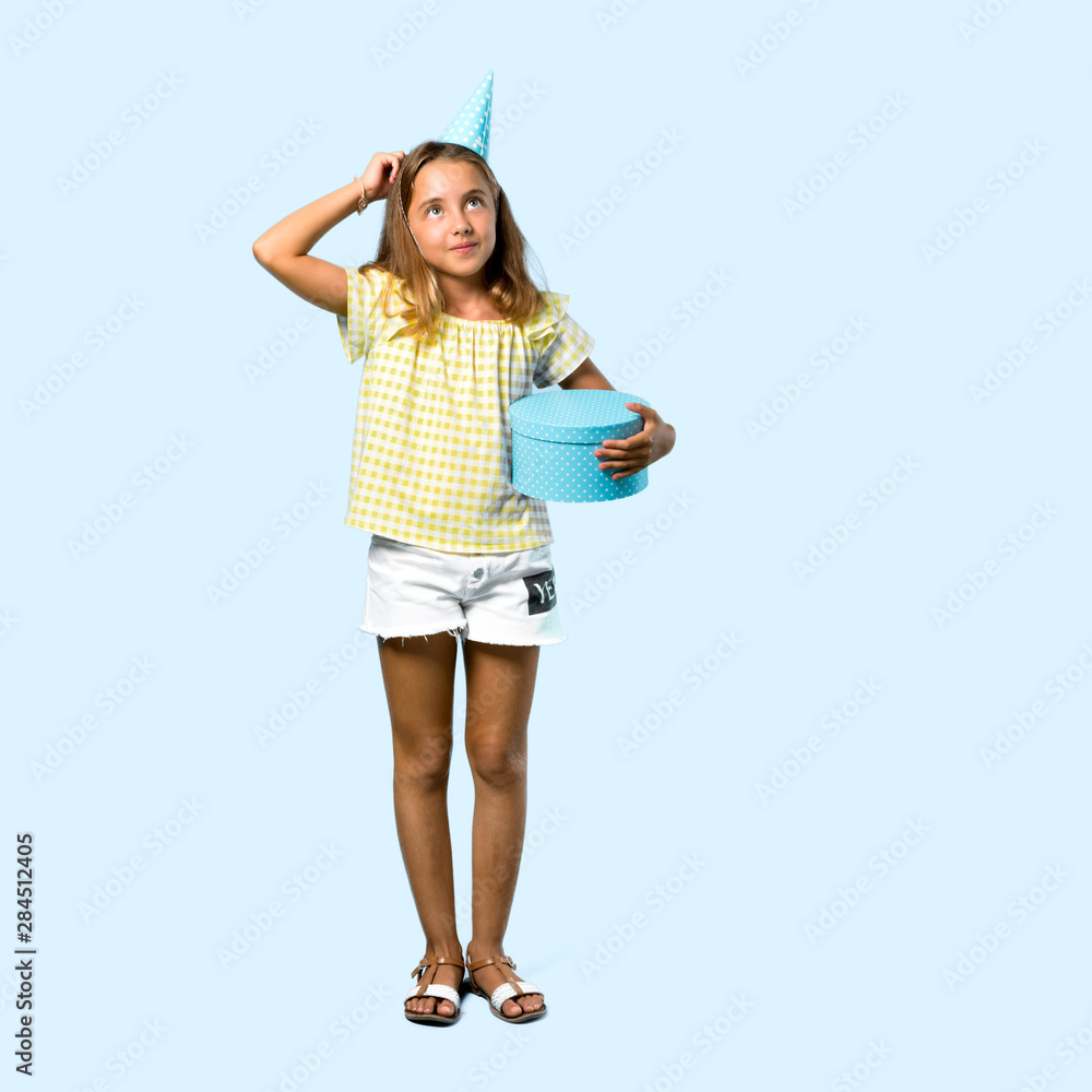 Full body of Little girl at a birthday party holding a gift standing and thinking an idea on blue background Full body of Little girl at a birthday party holding a gift standing and thinking an idea on blue background