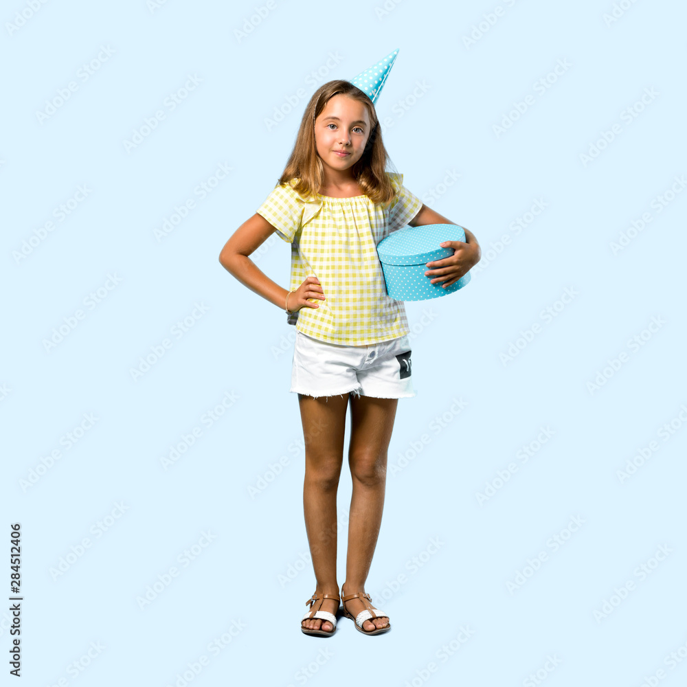 Full body of Little girl at a birthday party holding a gift posing with arms at hip on blue background Full body of Little girl at a birthday party holding a gift posing with arms at hip on blue background