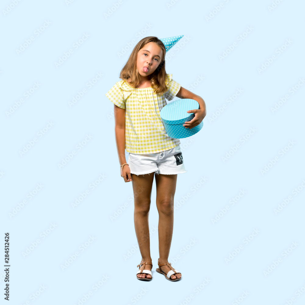Full body of Little girl at a birthday party holding a gift showing tongue at the camera having funny look on blue background Full body of Little girl at a birthday party holding a gift showing tongue at the camera having funny look on blue background