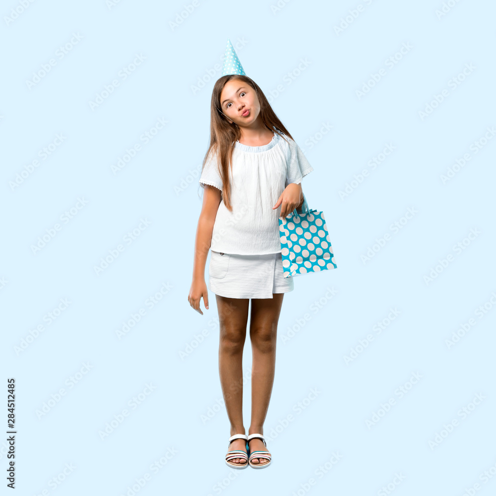 Full body of Little girl at a birthday party holding a gift bag makes funny and crazy face emotion on blue background Full body of Little girl at a birthday party holding a gift bag makes funny and crazy face emotion on blue background
