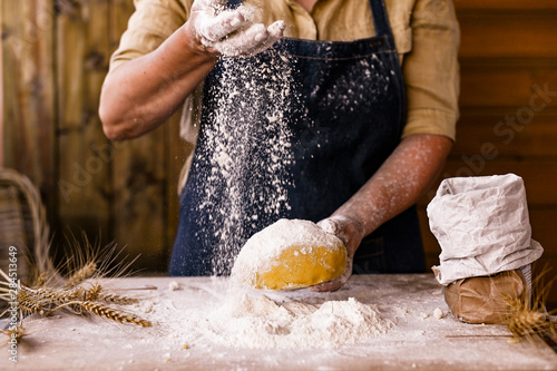 Women's hands, flour and dough. Levitation in a frame of dough and flour. A woman in an apron is preparing dough for home baking. Rustic style photo. Wooden table, wheat ears and flou.Emotional photo