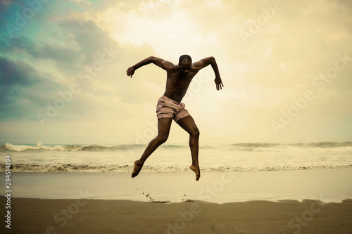 dramatic contemporary dance choreographer doing ballet beach workout . young attractive and athletic afro black American man dancing on sunrise jumping