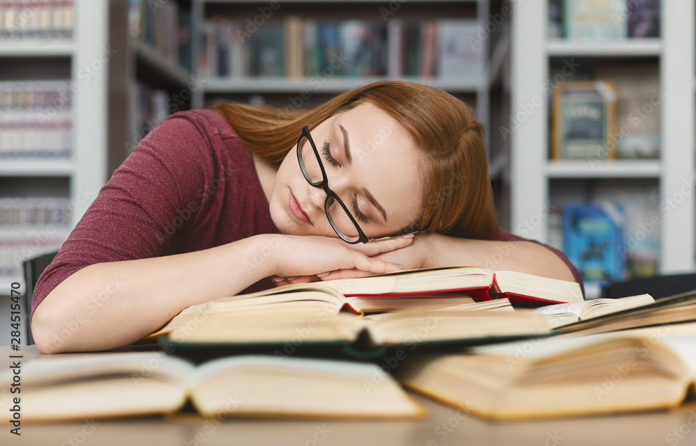Tired girl with glasses having nap on books in library Tired girl with glasses having nap on books in library