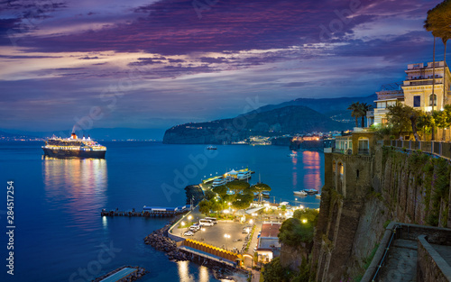 Sunset view of cliff coastline and illuminated marina in Sorrento, Italy