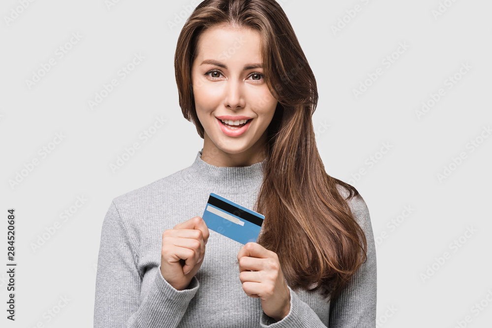 Young woman holding credit card. Isolated on grey background. Studio shot. Online shopping, e-commerce, internet banking, spending money, enjoying life concepts Young woman holding credit card. Isolated on grey background. Studio shot. Online shopping, e-commerce, internet banking, spending money, enjoying life concepts