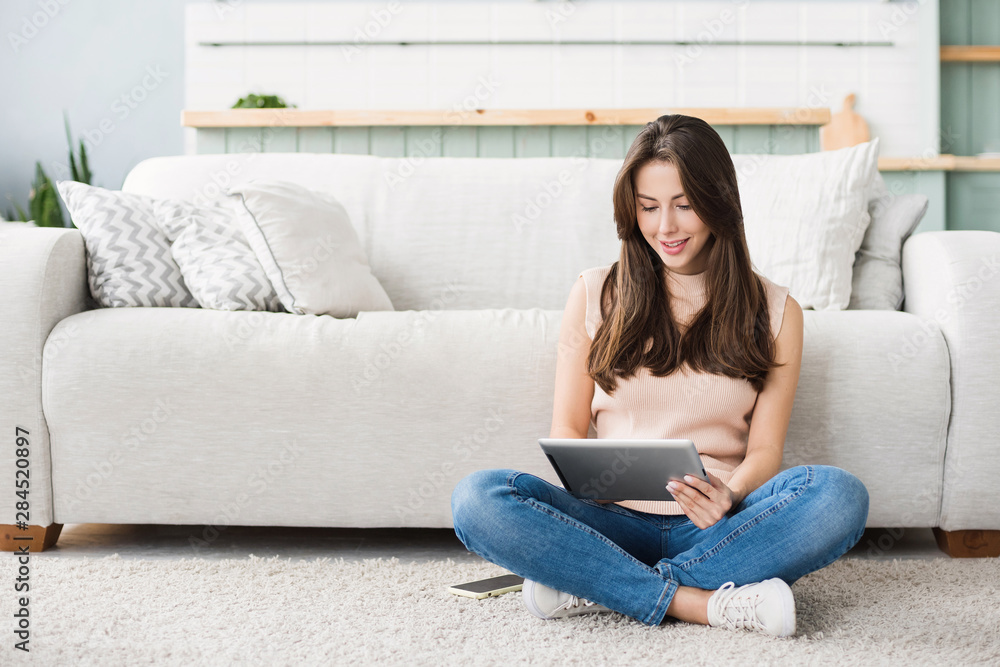 Beautiful young woman with digital tablet relaxing at home. Happy smiling girl sitting in living room using tablet pc. Resting, relaxation, technology concept Beautiful young woman with digital tablet relaxing at home. Happy smiling girl sitting in living room using tablet pc. Resting, relaxation, technology concept