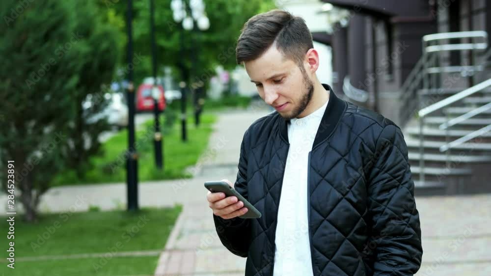 Handsome bearded man uses the mobile phone on the street in, typing text, chatting with friends Handsome bearded man uses the mobile phone on the street in, typing text, chatting with friends