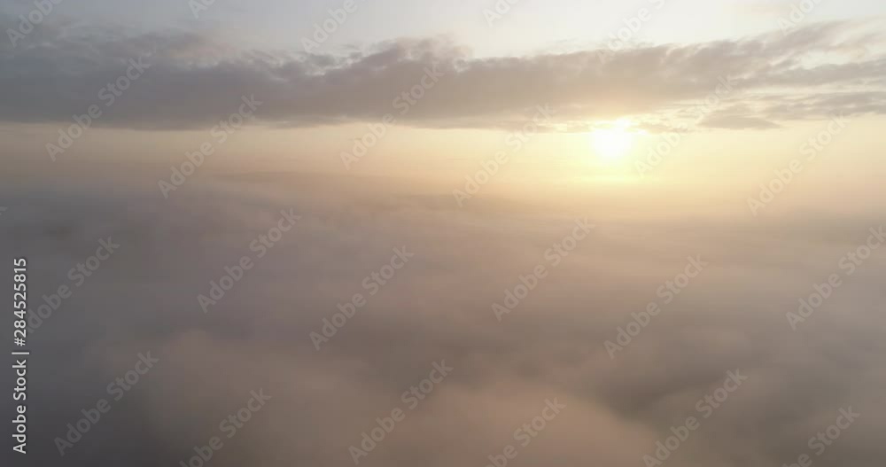 Aerial shot of flying over the clouds towards sunrise.