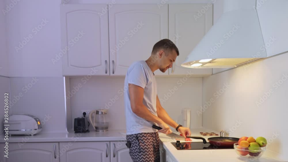 A young man in his kitchen, cut tomatoes and fry it. Man prepares food and dances. A young man in his kitchen, cut tomatoes and fry it. Man prepares food and dances.