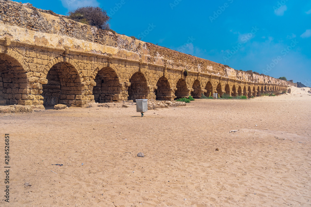 Ruins of the Roman aqueduct arches on the beach of Caesarea Israel with blue see and sky