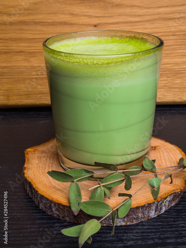 a cup of hot milk green motcha latte coffee with branch on wooden background, copy space
