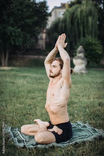 Yoga at park. Bearded man in lotus pose sitting on green grass. Concept of calm and meditation. photo